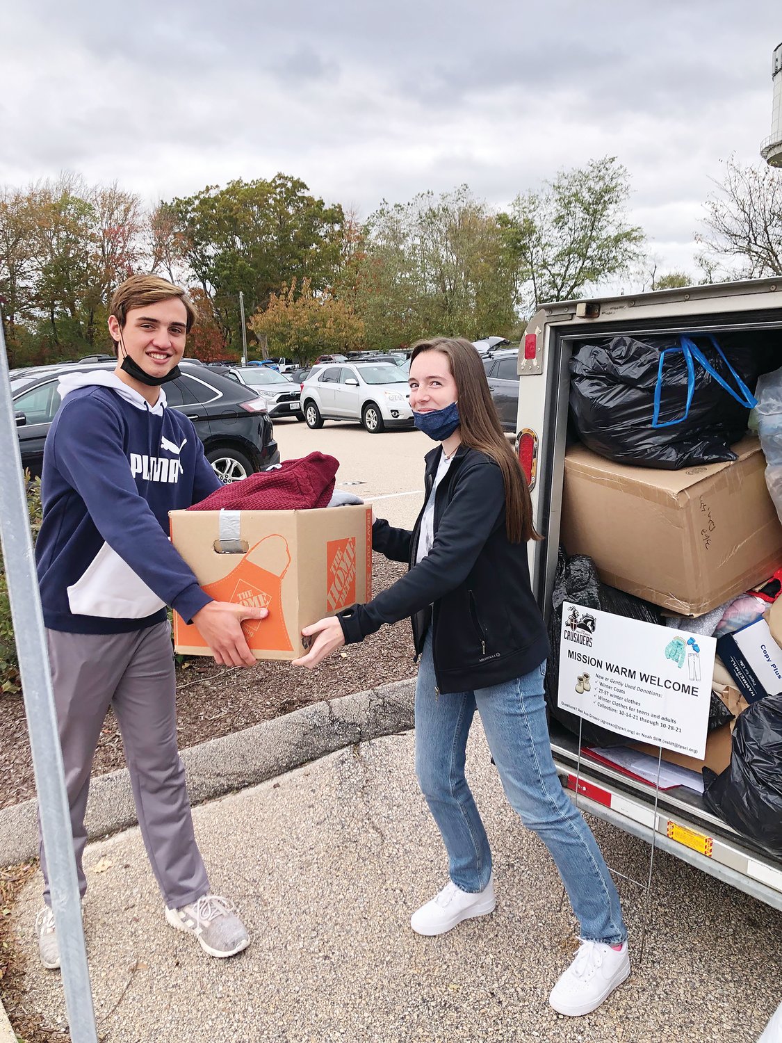 Prout student Ben Leal hands Operation Warm Welcome Administrator Ava Grosso, a Prout senior, a box of clothing items donated to the initiative, which will provide clothing for Afghan refugees currently at Fort McCoy, Wisconsin, as they wait to be resettled in the U.S.